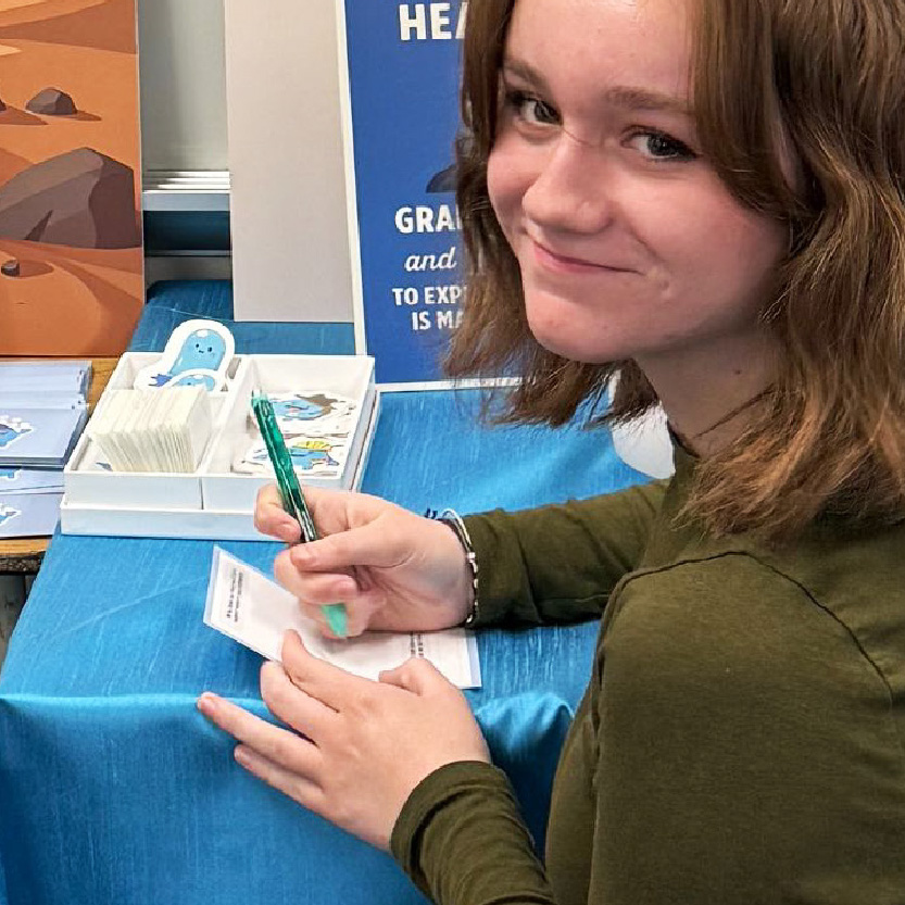 A smilling girl with pen and paper in her hands.